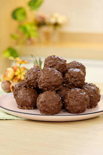 Prato branco com bombons crocantes de wafer cobertos por chocolate, sobre fundo desfocado.
