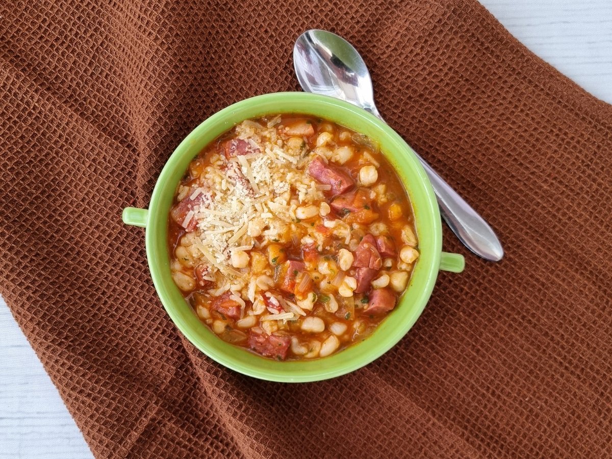 Tigela com canjica salgada com calabresa, queijo ralado e ervas, servida sobre mesa marrom.