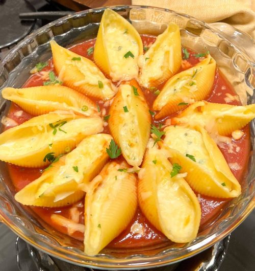 Travessa com conchiglioni recheados de queijo e cobertos por molho vermelho e cebolinha.