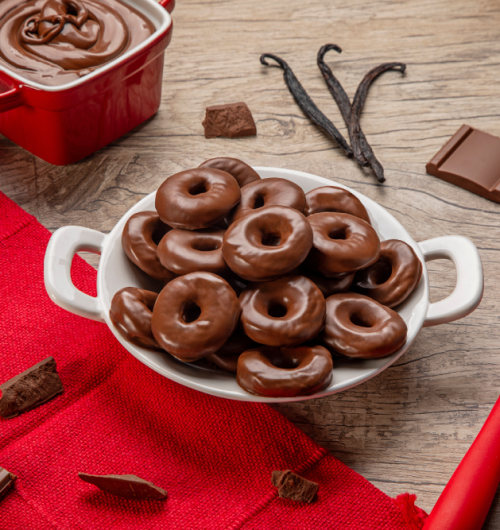Prato branco com donuts sabor chocolate ao leite, sobre mesa de madeira.