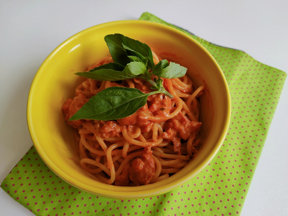 Prato de espaguete, coberto com molho vermelho, linguiça toscana e manjericão fresco.