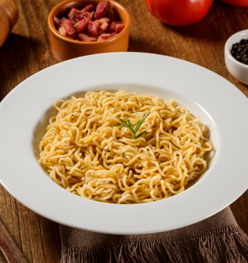 Tigela de macarrão instantâneo sabor galinha, com alecrim, sobre mesa de madeira.