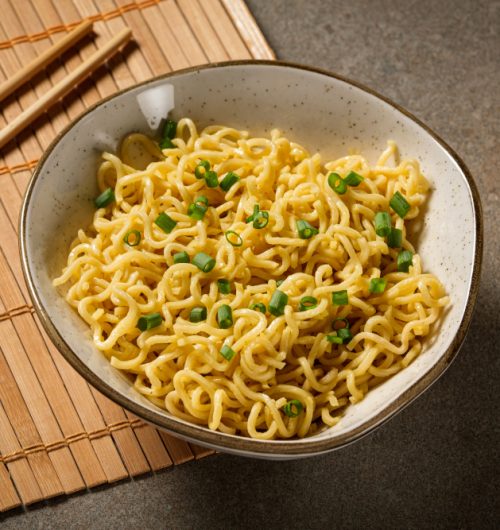 Tigela de macarrão instantâneo sabor galinha, com cebolinha, sobre mesa de madeira.
