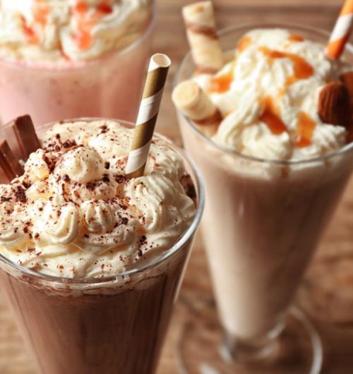 Copo de vidro com milkshake de biscoito recheado, servido com canudo sobre mesa de madeira.