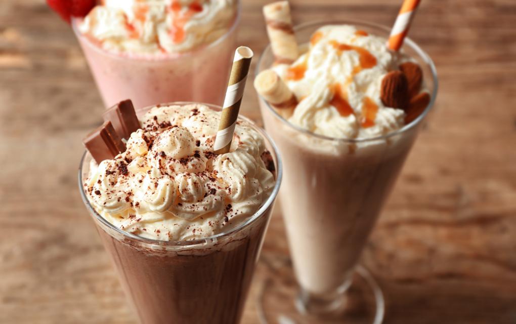 Copo de vidro com milkshake de biscoito recheado, servido com canudo sobre mesa de madeira.