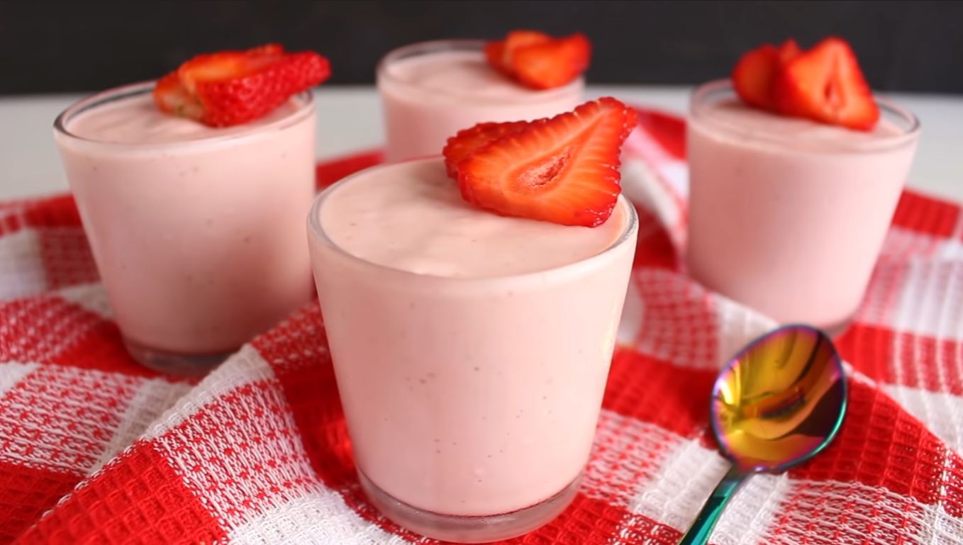 Taça com mousse de morango com rosca de calda, decorado com morangos, sobre fundo desfocado.