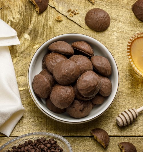 Pedaços de pão de mel cobertos com chocolate, dispostos em pote branco sobre mesa de madeira.