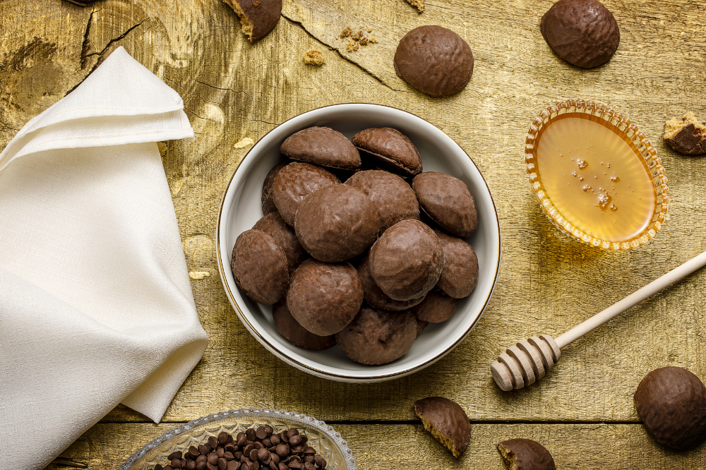 Pedaços de pão de mel cobertos com chocolate, dispostos em pote branco sobre mesa de madeira.