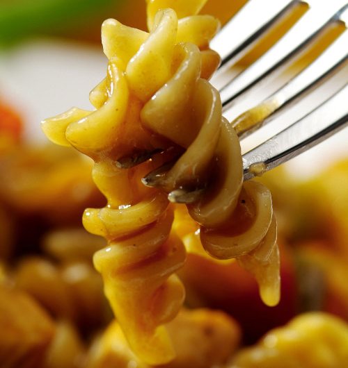 Garfo segurando macarrão parafuso coberto em molho, sobre fundo desfocado