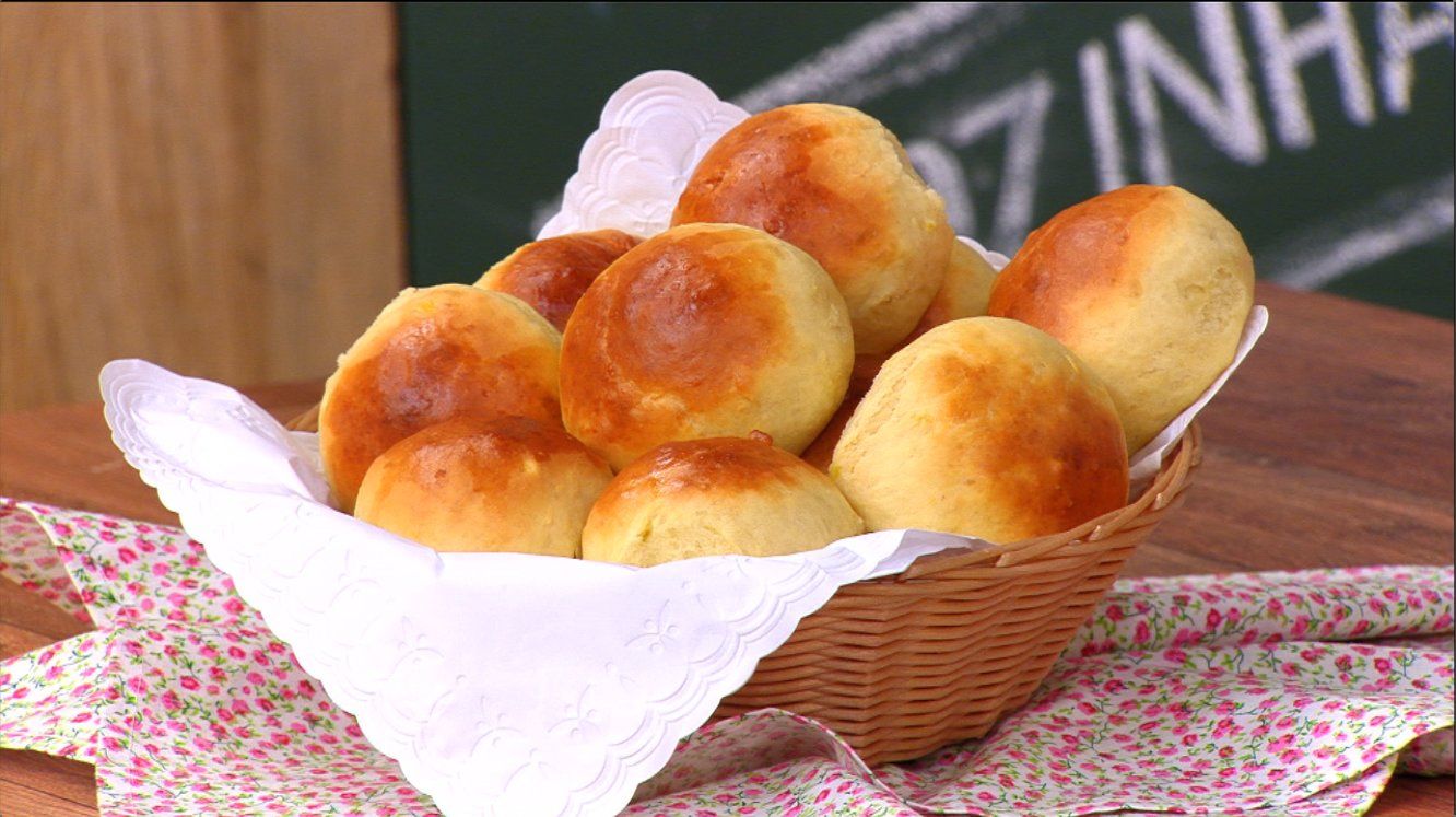 Cesta de pãozinhos de batata doce dourados, disposta sobre mesa de madeira.