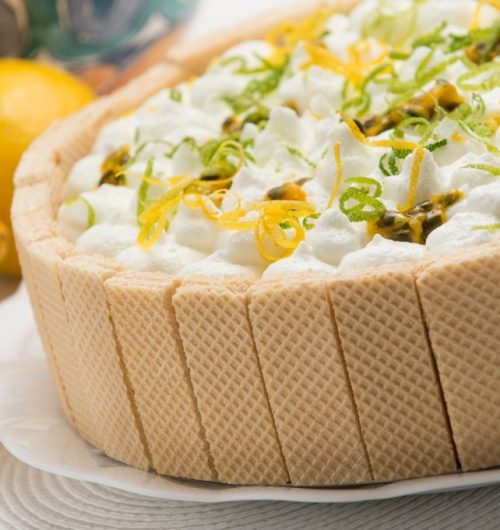 Torta com camadas de wafer e creme de limão, servida em prato branco sobre fundo desfocado.