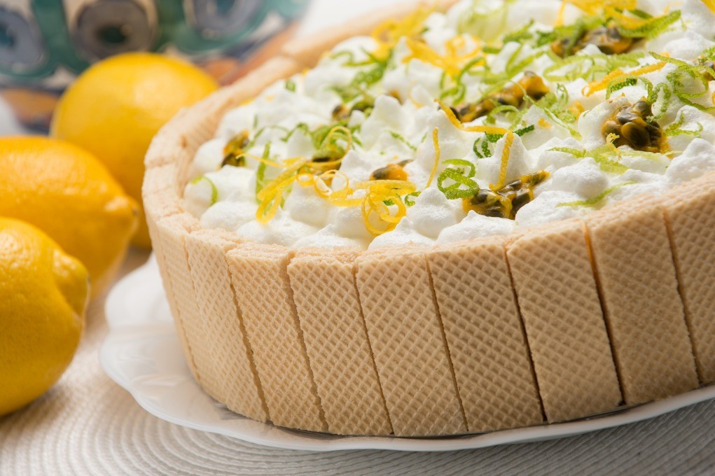 Torta com camadas de wafer e creme de limão, servida em prato branco sobre fundo desfocado.