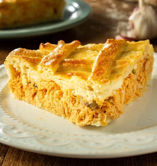 Fatia de torta de frango com crosta feita de biscoito Ninfa, em prato sobre mesa de madeira.