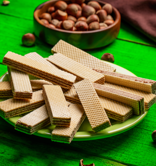 Wafer sabor chocolate com avelã dispostos em prato, sobre fundo verde.