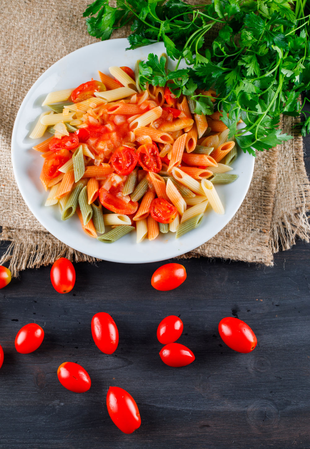 Prato de macarrão penne vegetias com molho de tomate e salsa, servido em prato branco, sobre mesa de madeira.
