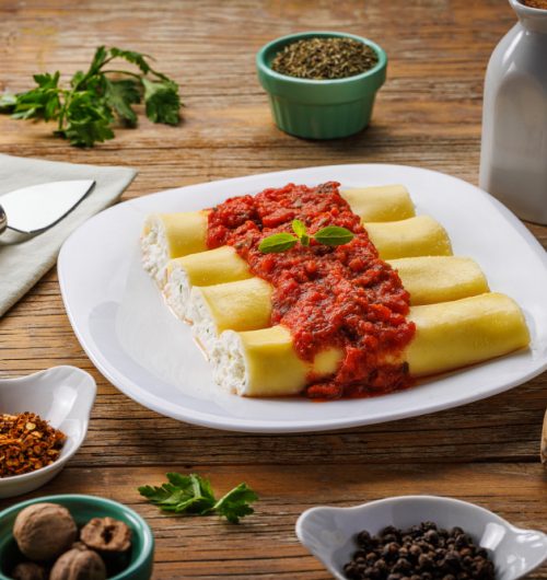 Prato de macarrão canelloni recheados com patê branco e cobertos em molho vermelho.